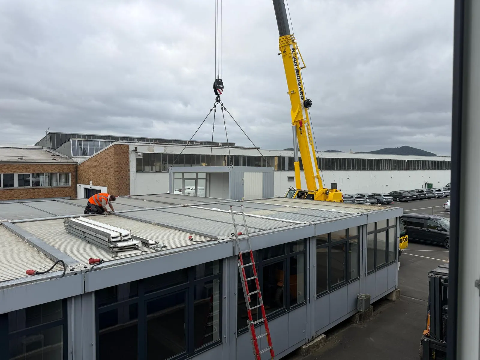 Autokran hebt ein Containermodul über ein Flachdach